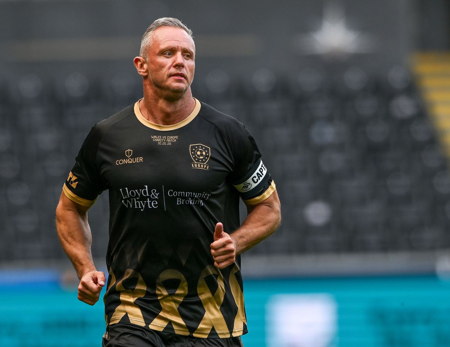 Male footballer in black and gold kit jogging on pitch during a match.