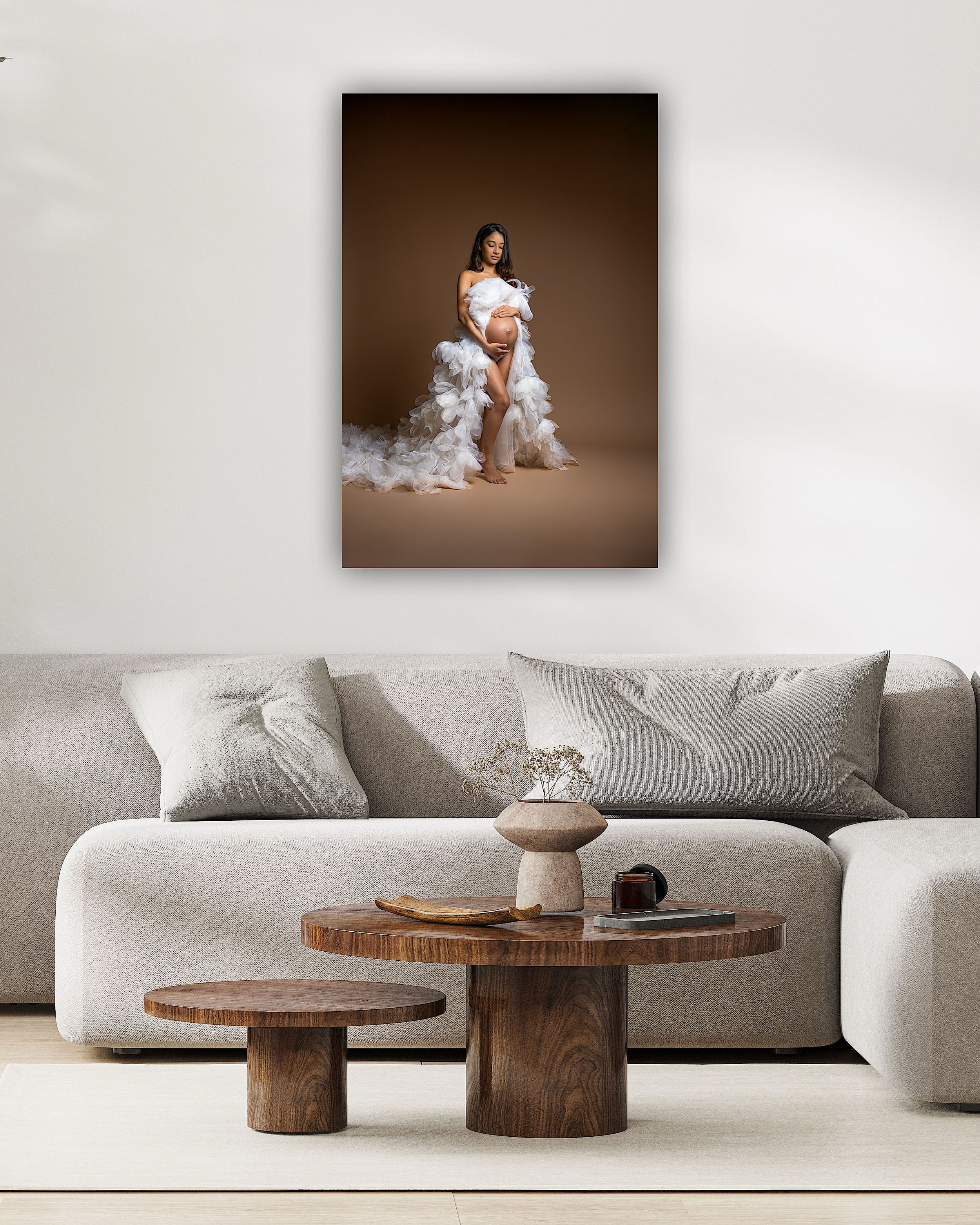 Pregnant woman in white ruffled gown posed elegantly, displayed as canvas wall art above a modern living room sofa.