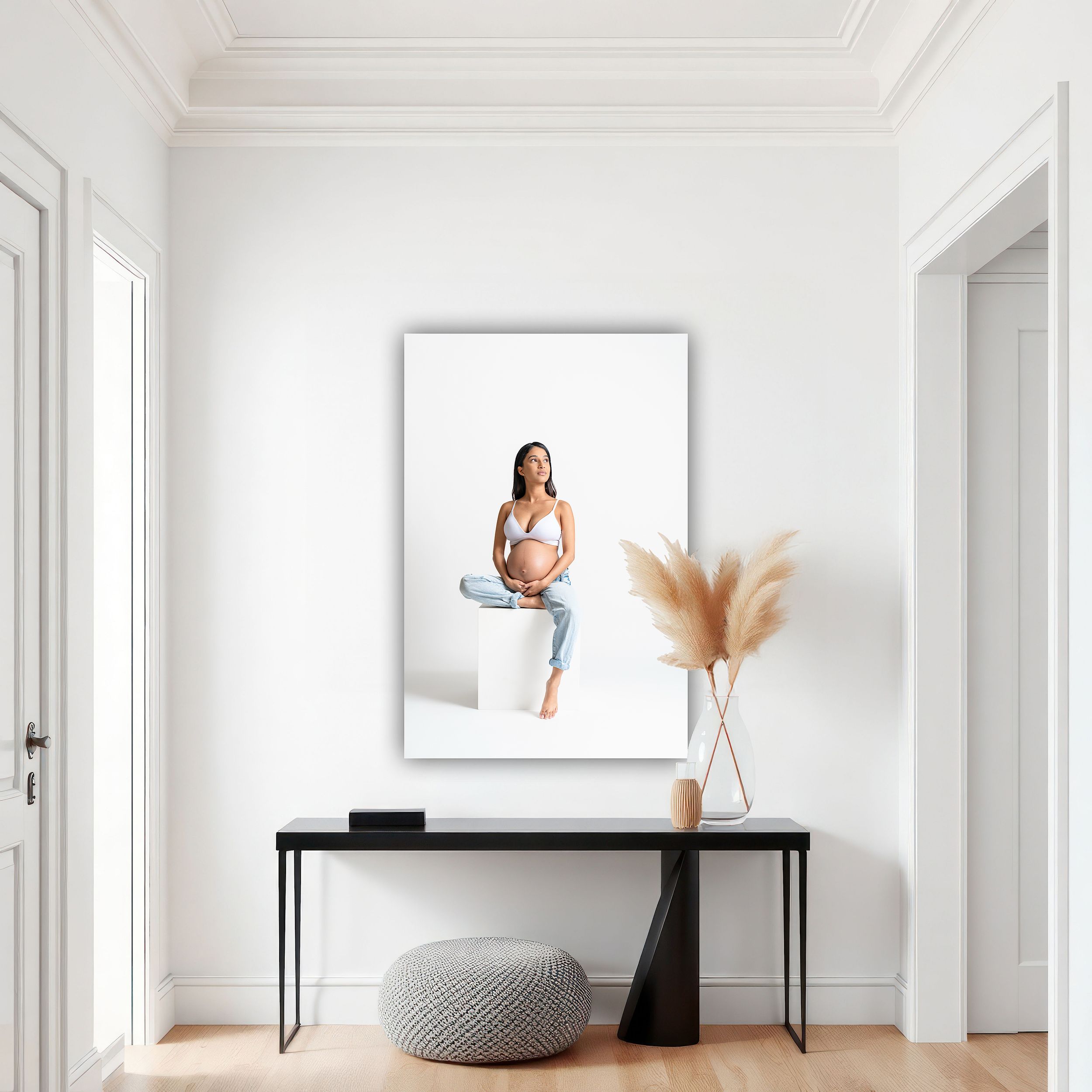 Pregnant woman in white crop top and jeans sitting on white cube, displayed as large wall art in modern hallway.
