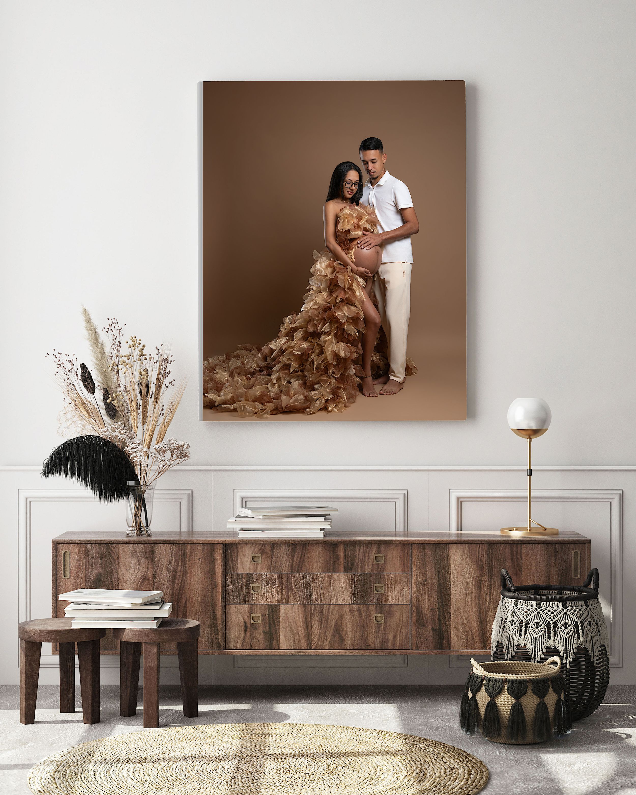 A couple poses for a maternity portrait, displayed as canvas wall art above a wooden sideboard in a modern living room.