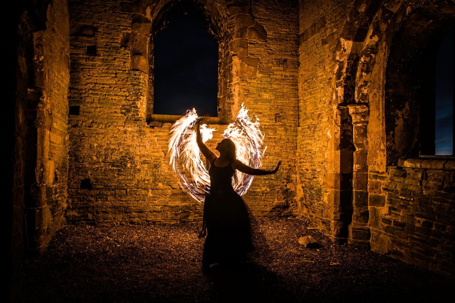 Silhouette of a person creating a glowing light orb at night near ancient stone ruins.