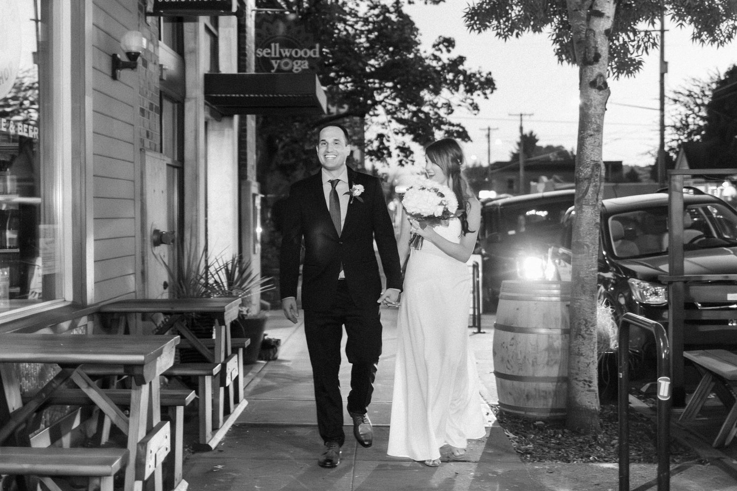 Black and white photo of a bride and groom holding hands walking outside a Sellwood yoga studio on their wedding day.