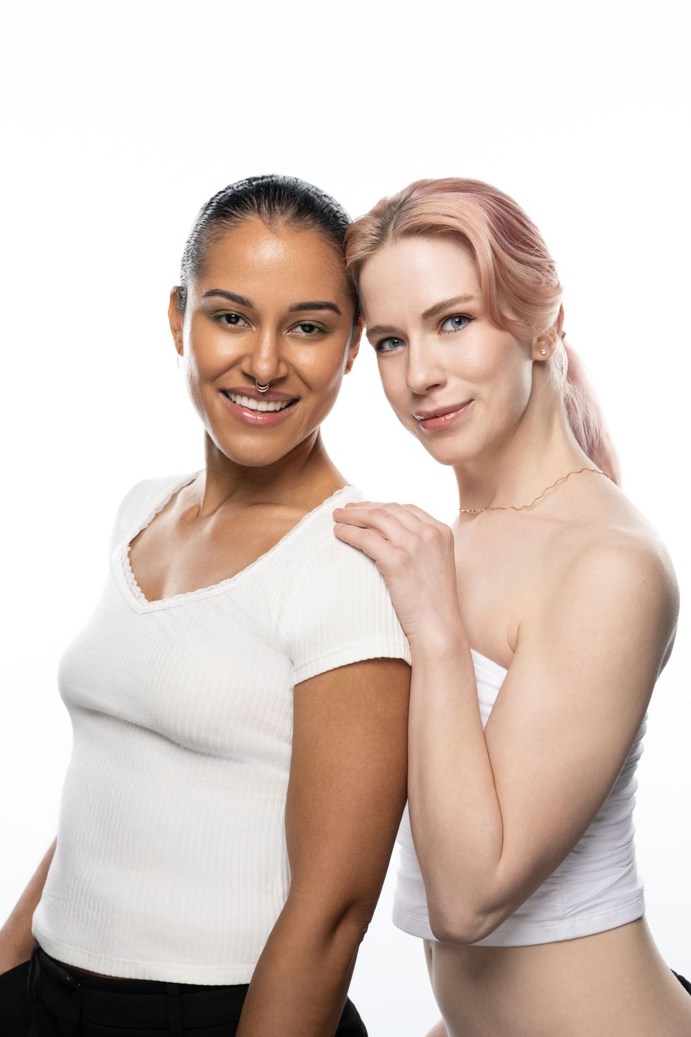 Two smiling women in white tops pose together against a white background in a studio portrait.
