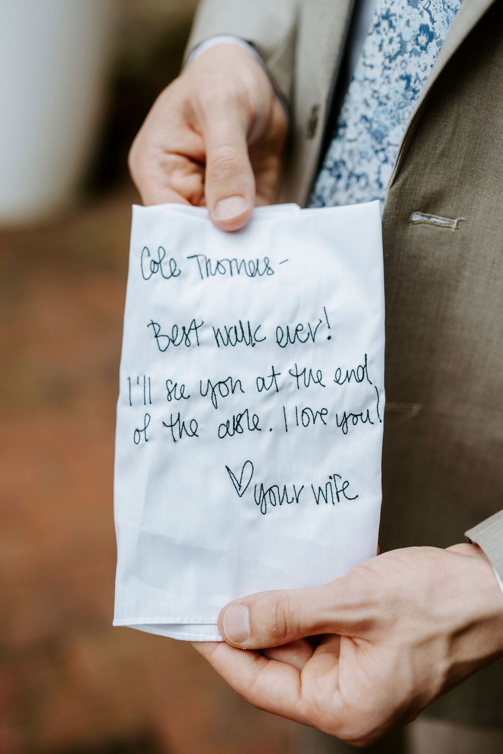 Groom holds a handwritten note from his bride reading Best walk ever, I'll see you at the end of the aisle, love your wife.