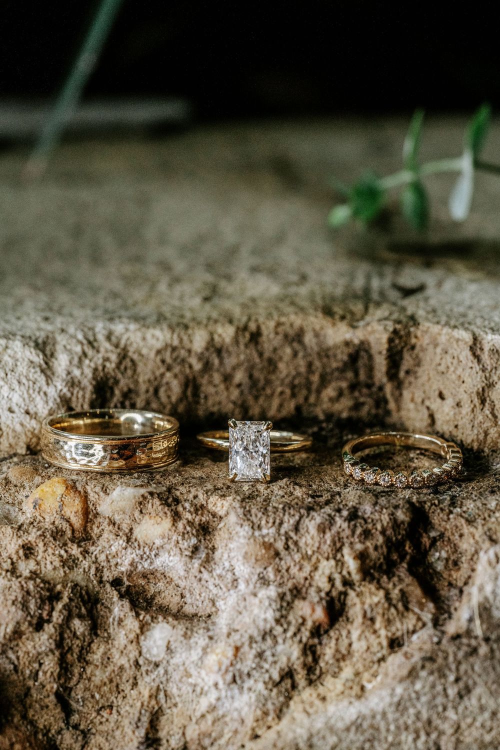 Three gold wedding rings with diamonds displayed on a rustic stone surface in natural light.