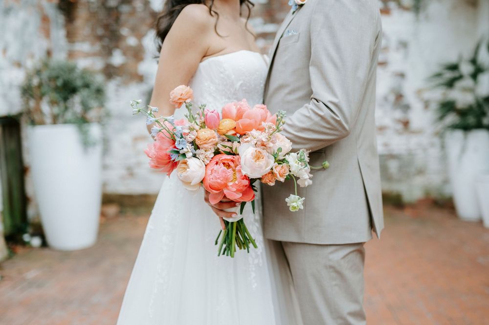 Close-up of bride and groom embracing, showcasing a lush coral and white wedding bouquet.