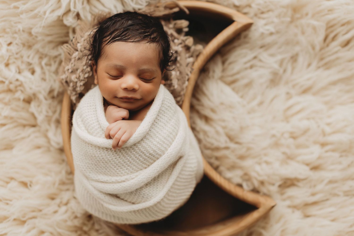 Newborn baby sleeping peacefully wrapped in a soft gray knit swaddle blanket on a white background.