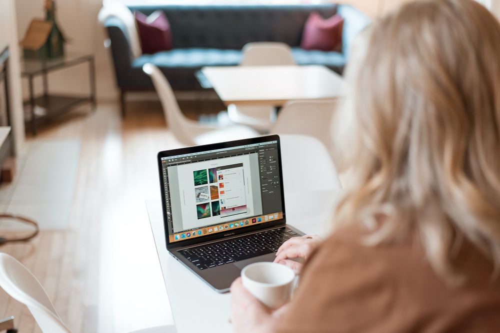 Over-shoulder view of laptop screen and workspace with coffee cup in living room setting.