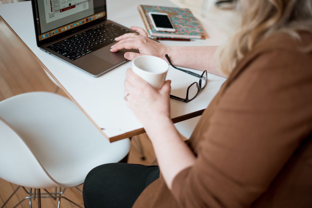 Person working on laptop with coffee cup and glasses on white desk.