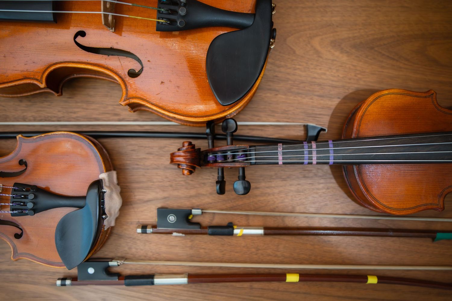 Two wooden violins with bows arranged on a hardwood surface, showcasing classic string instruments for music.