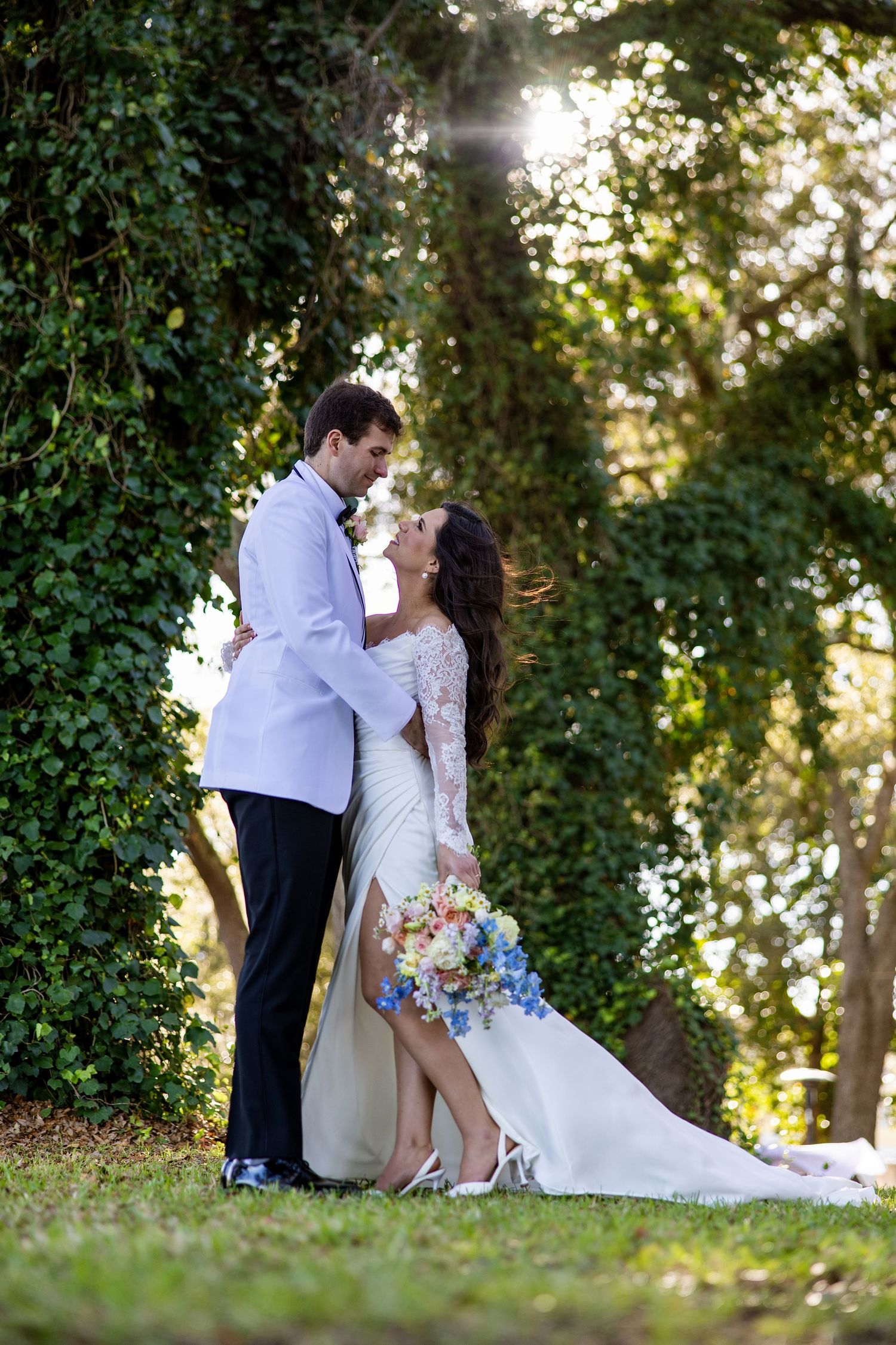 Bride and groom share a romantic moment in a lush garden, bride holding a colorful bouquet in a white lace gown in Pensacola, florida