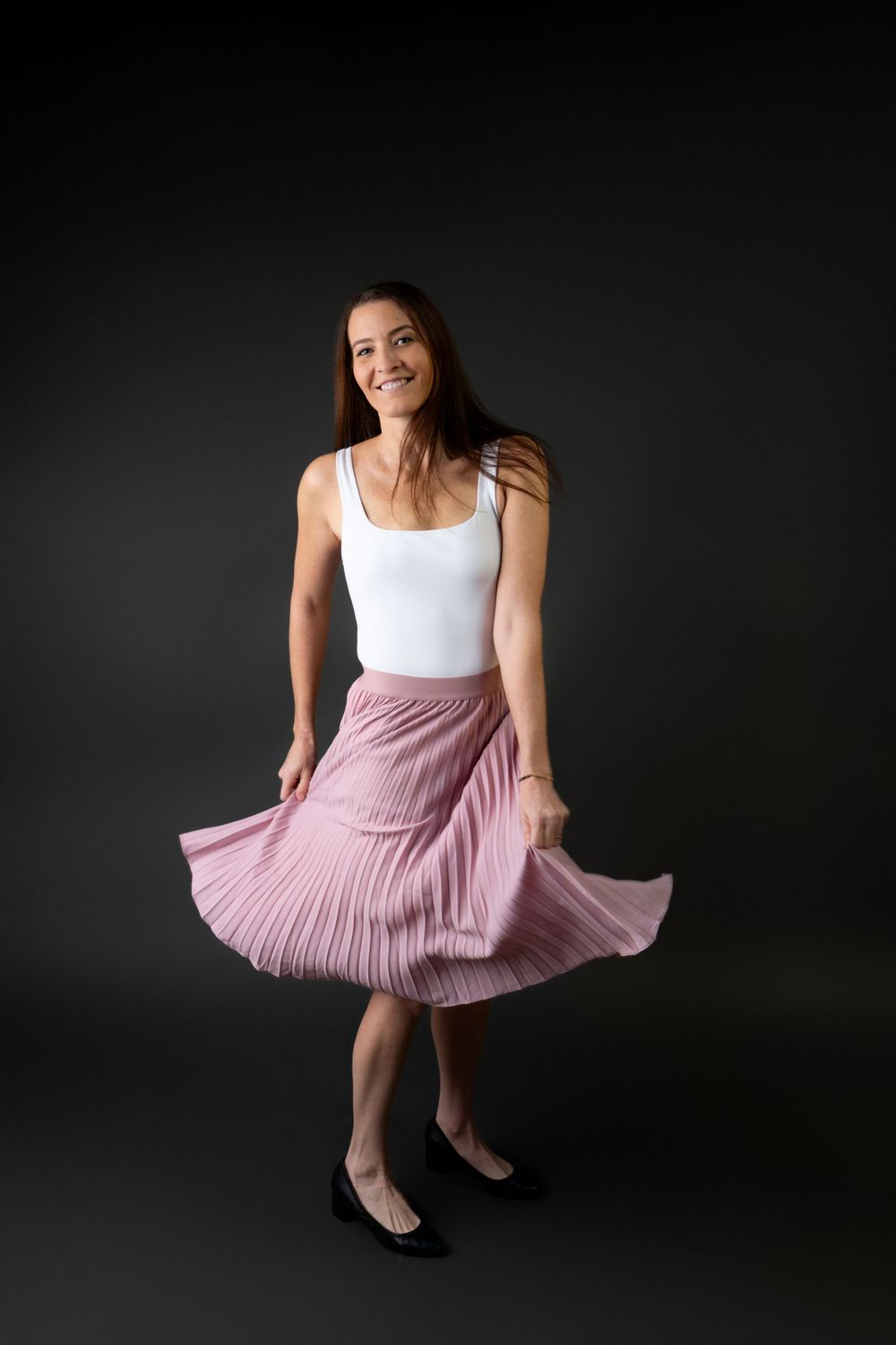 Studio portraits showing poses in a white top and pink pleated skirt.