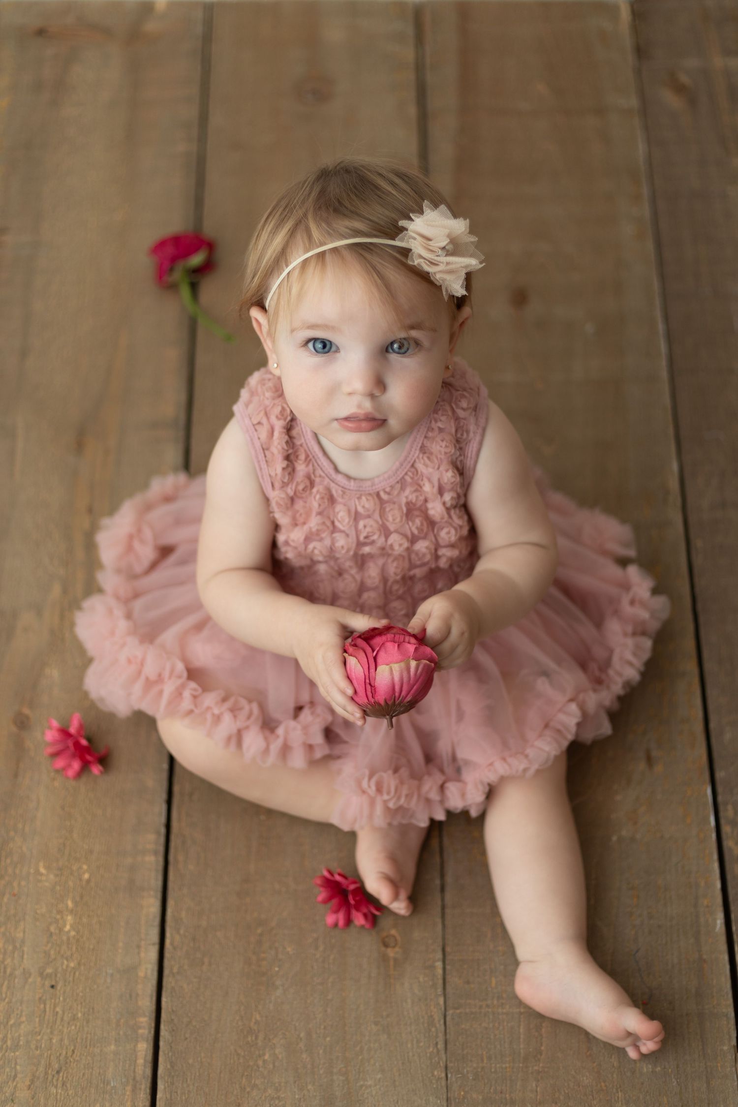 Sweet portrait in pink dress with flower on wooden floor.