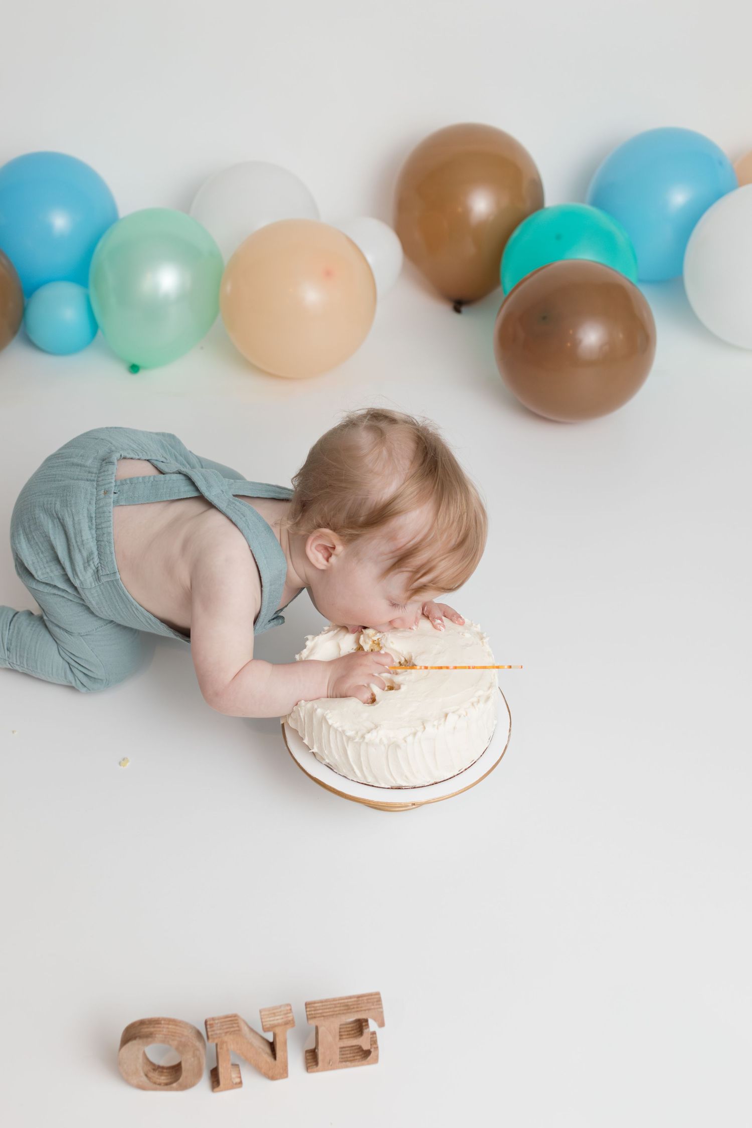 First birthday cake smash session with balloons and wooden 'ONE' letters on white background.