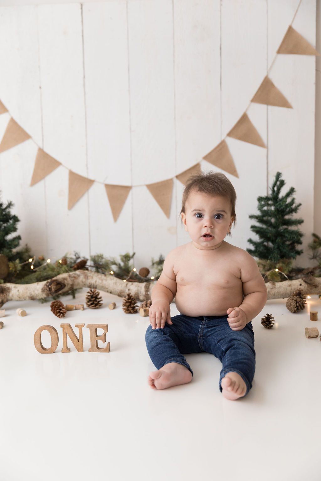 A first birthday setup with rustic decor featuring wooden 'ONE' letters, pine cones and burlap bunting.