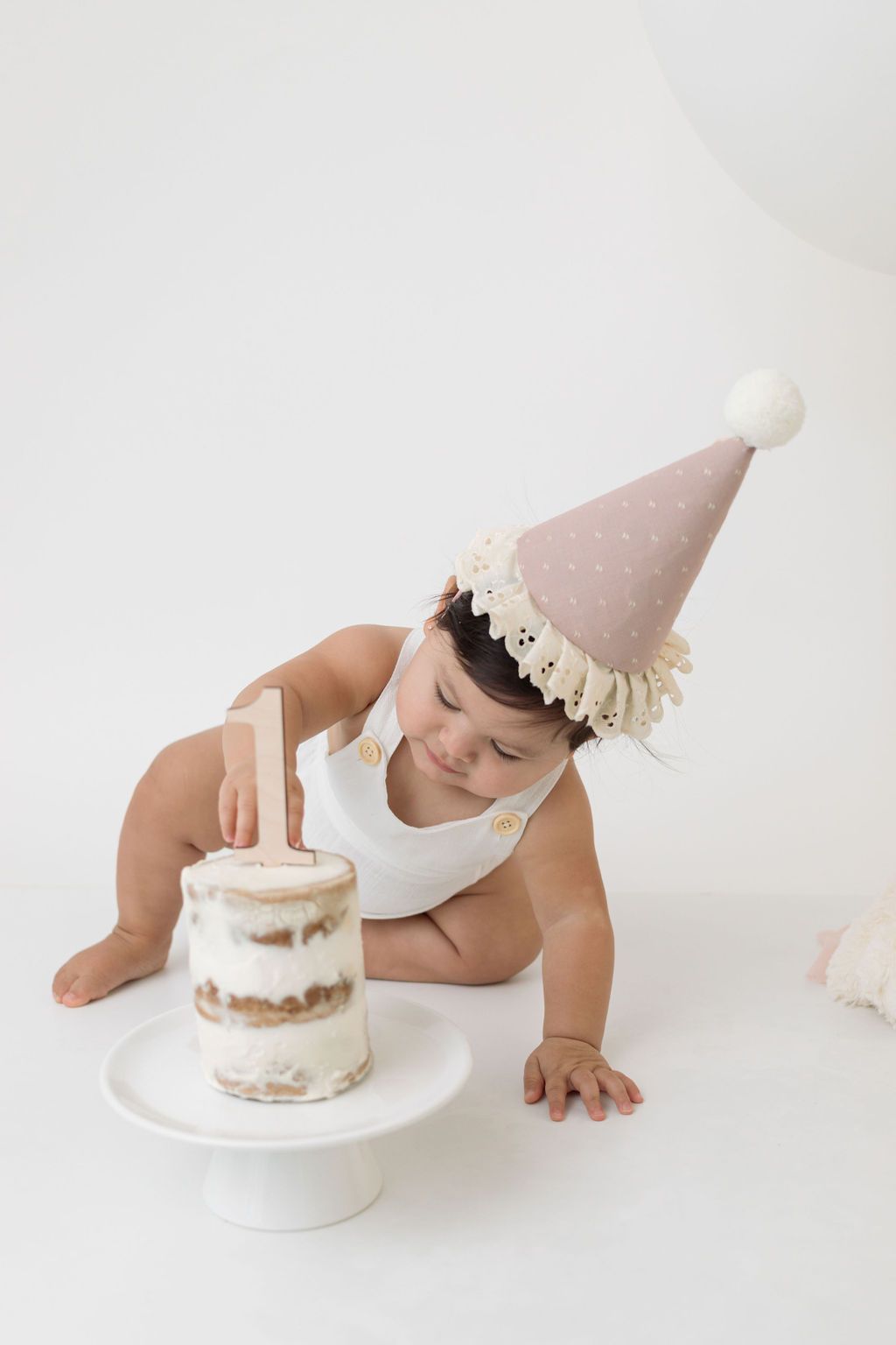 Cake smash setup with pink party hat and small naked cake.