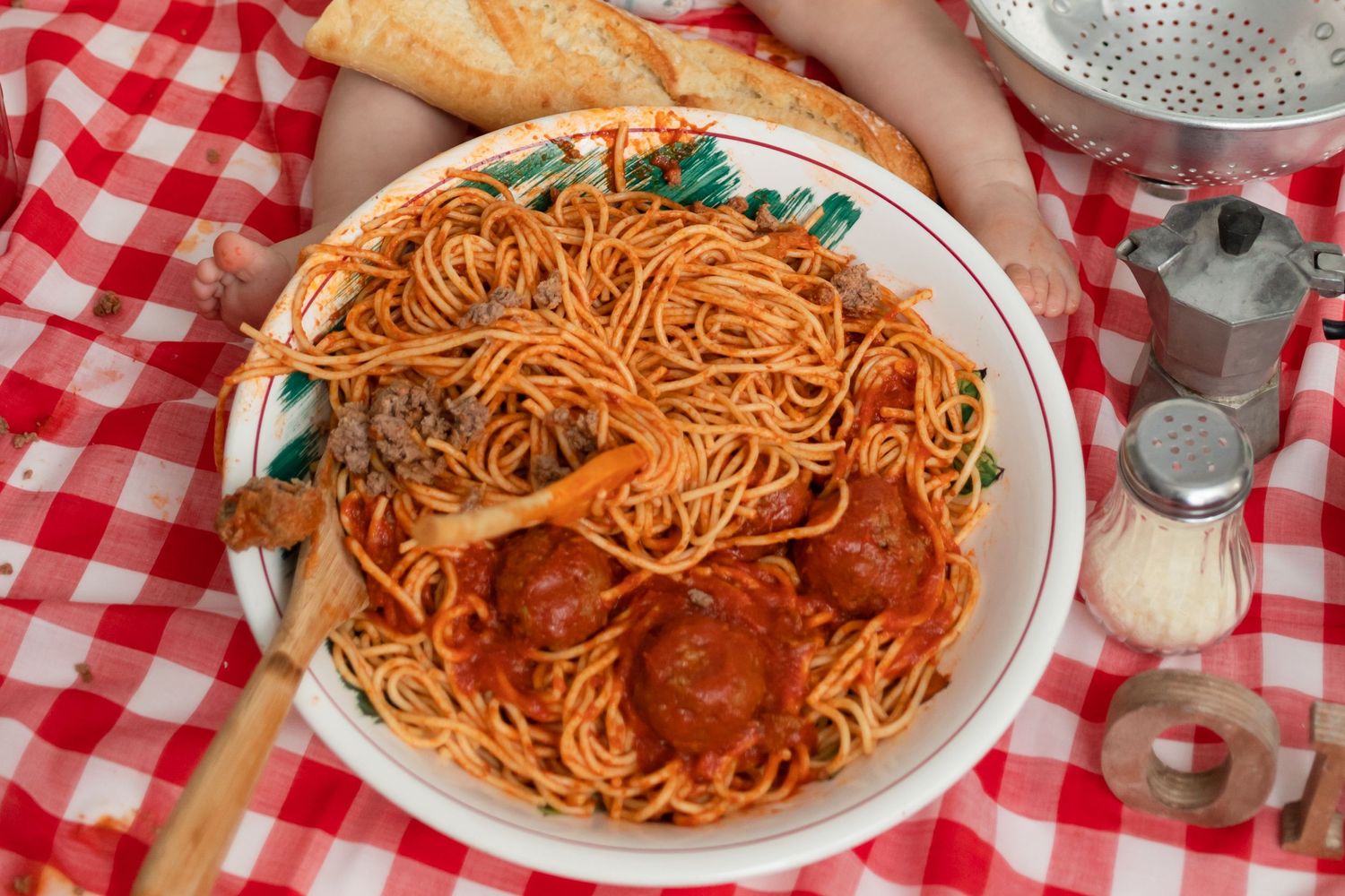 A plate of spaghetti and meatballs served on a red and white checkered tablecloth with breadsticks.