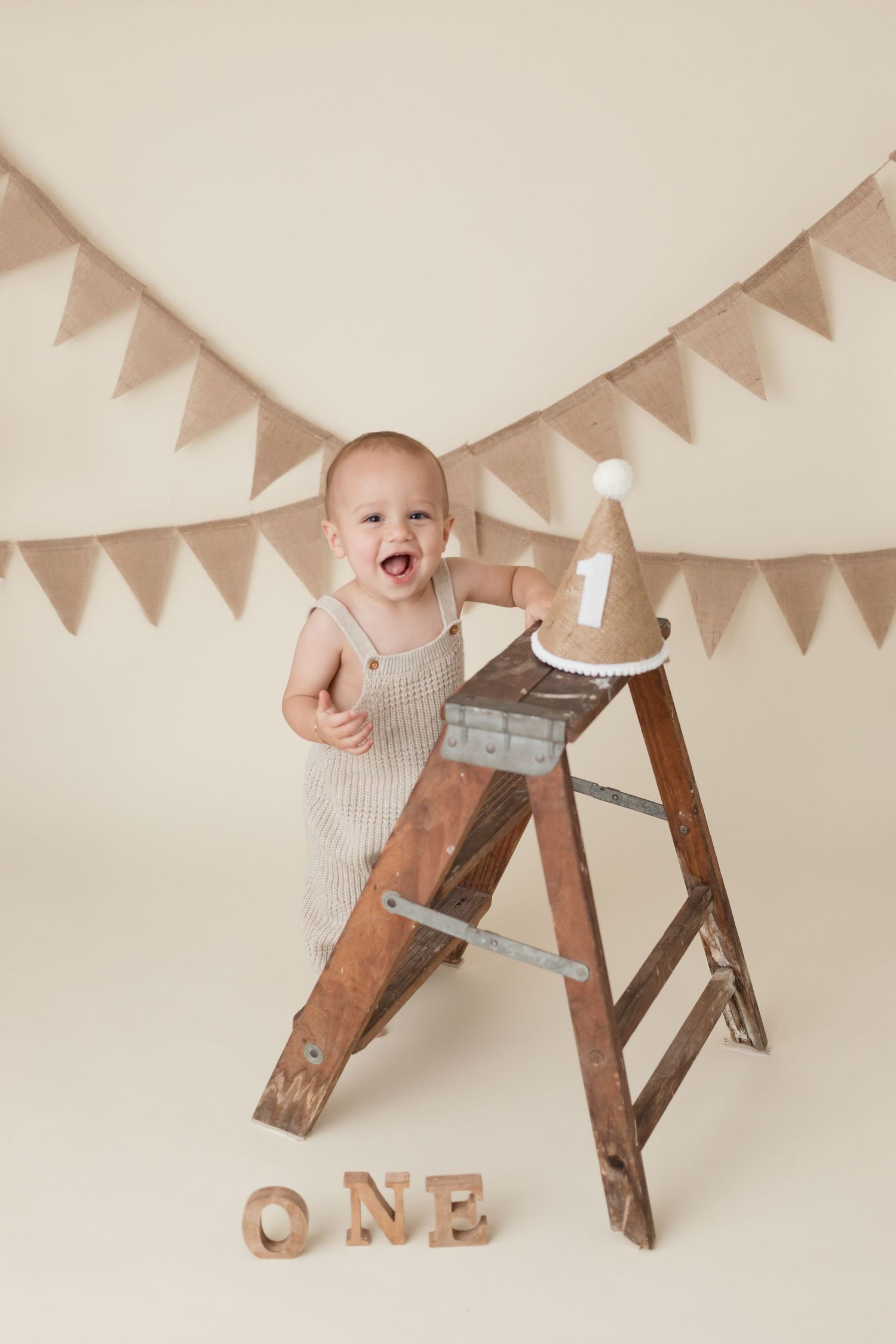 A vintage ladder decorated for a first birthday photoshoot with burlap bunting and wooden letters.
