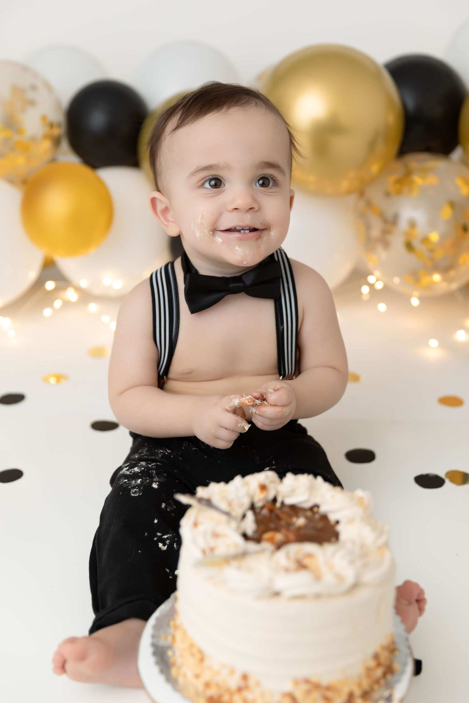 First birthday celebration with white cake and black and gold balloon decorations in the background.