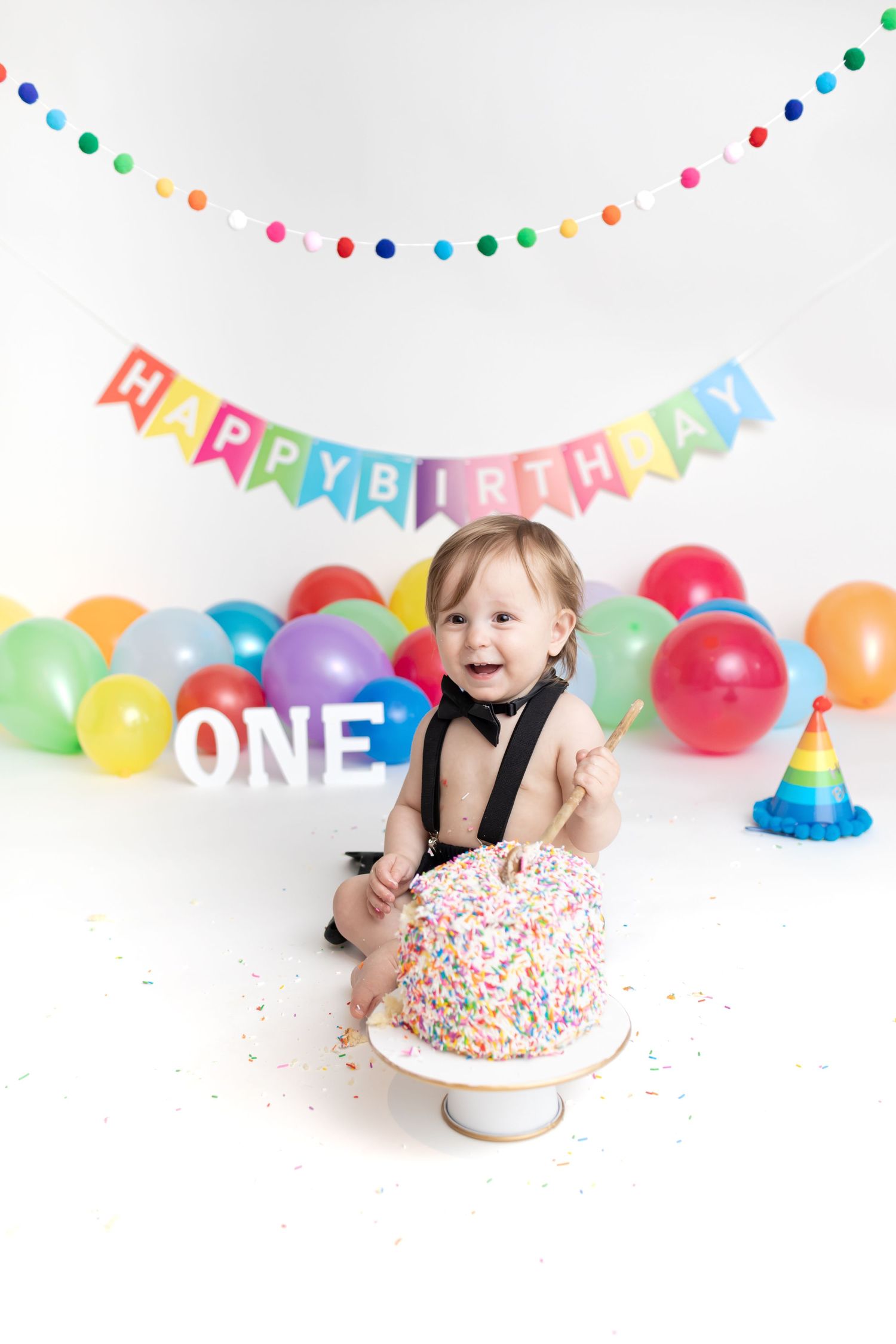 Festive birthday setup with rainbow balloons, colorful bunting, and a sprinkle-covered cake.