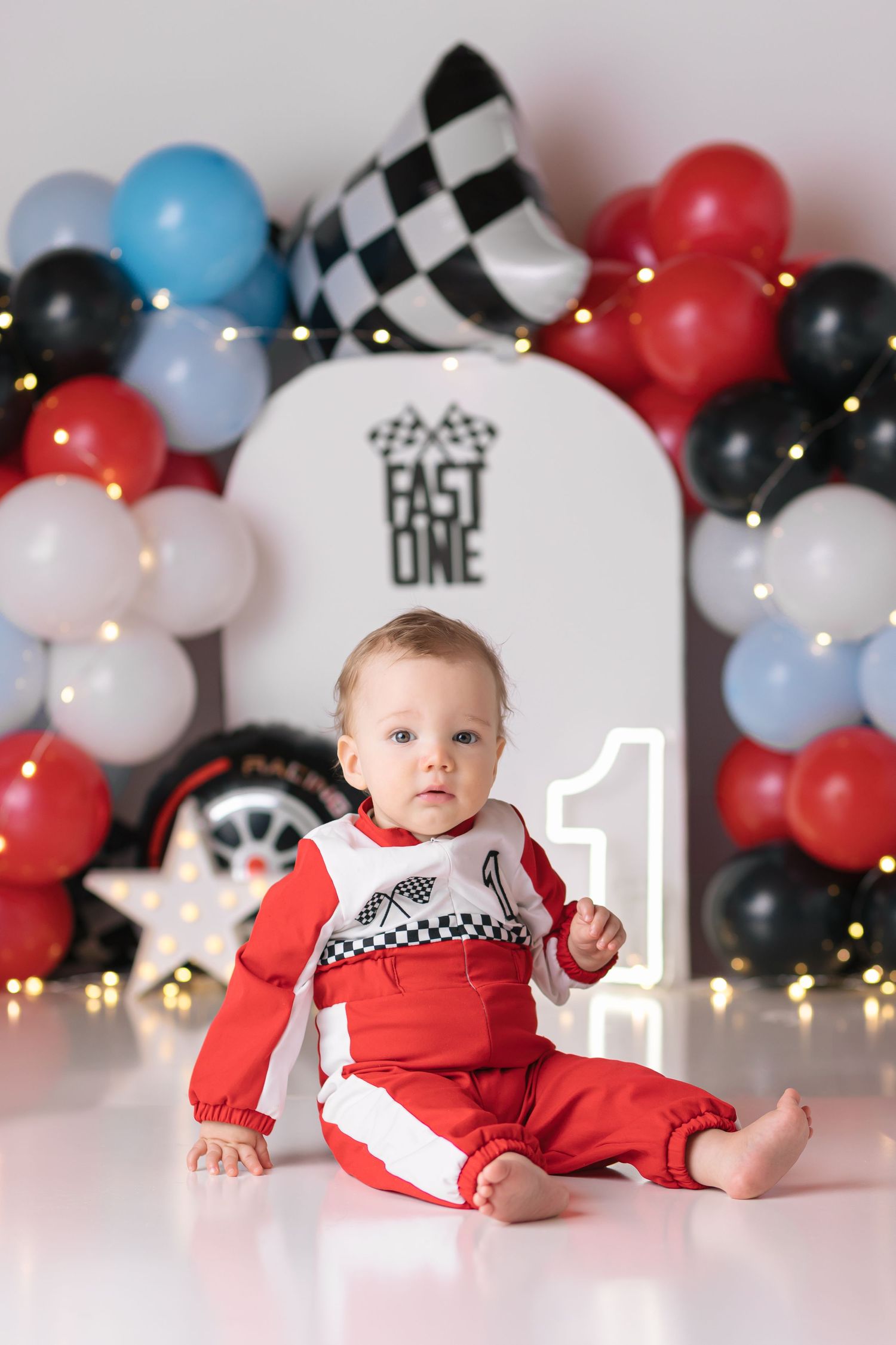 First birthday celebration setup with red, black and blue balloon arch and racing theme decor.