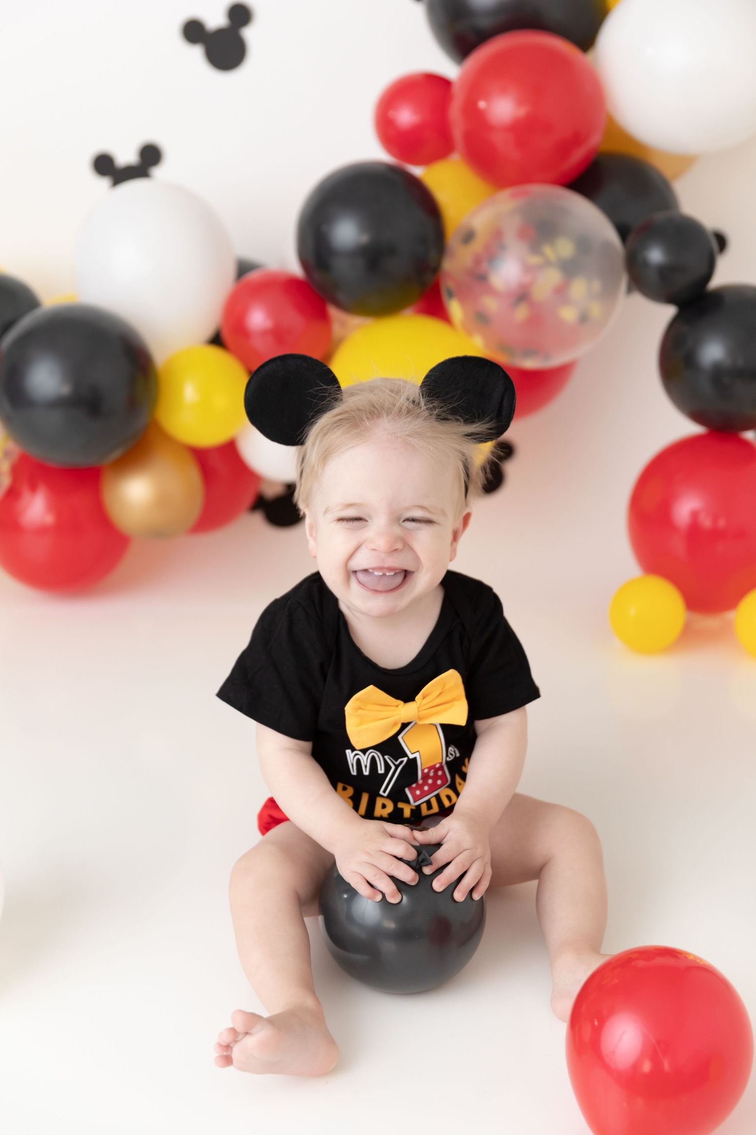 Mickey Mouse themed birthday photo setup with balloons in black, red, yellow and gold creating a festive backdrop.
