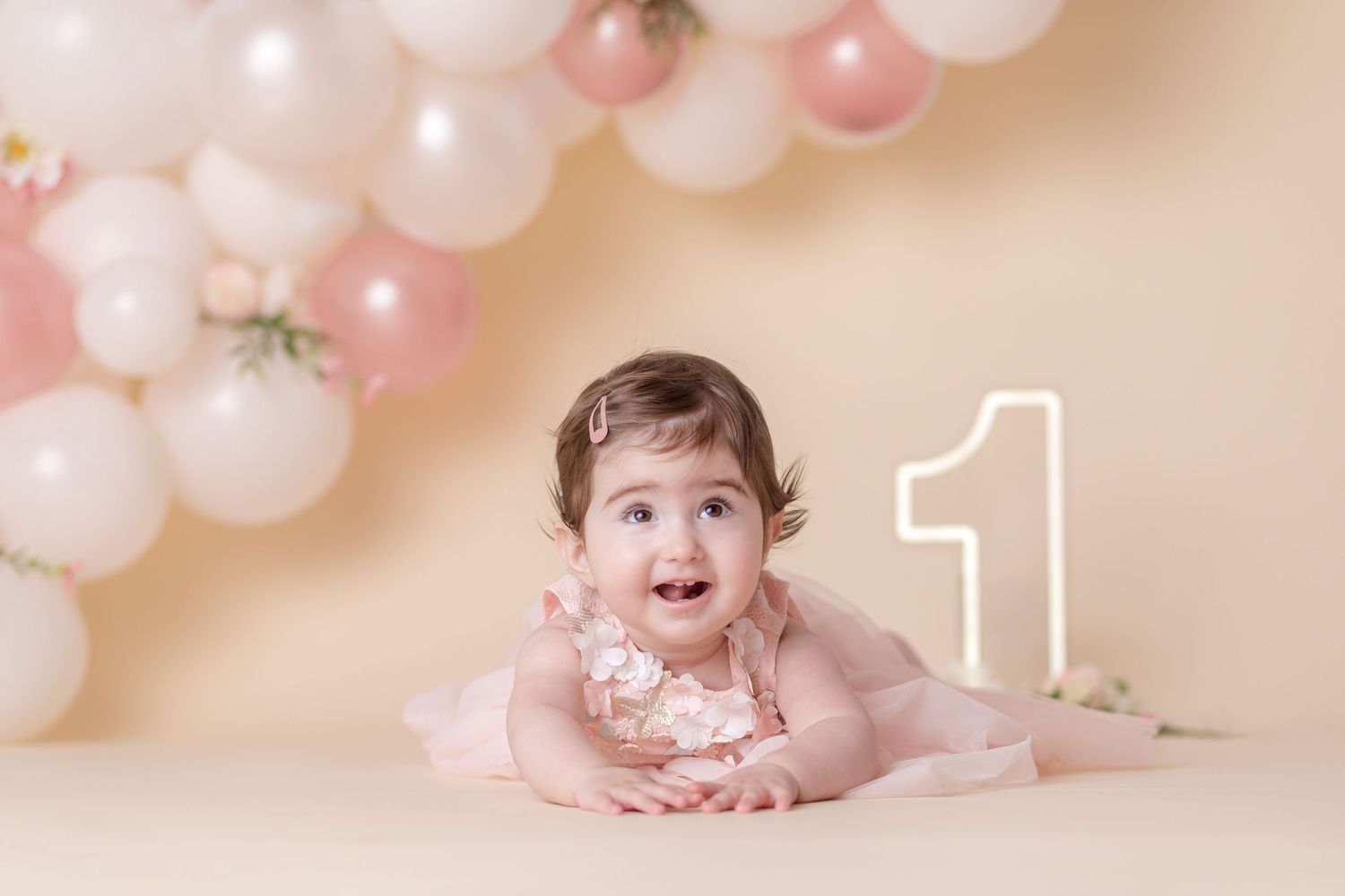 First birthday photo setup with pink and white balloon arch and number one decoration.