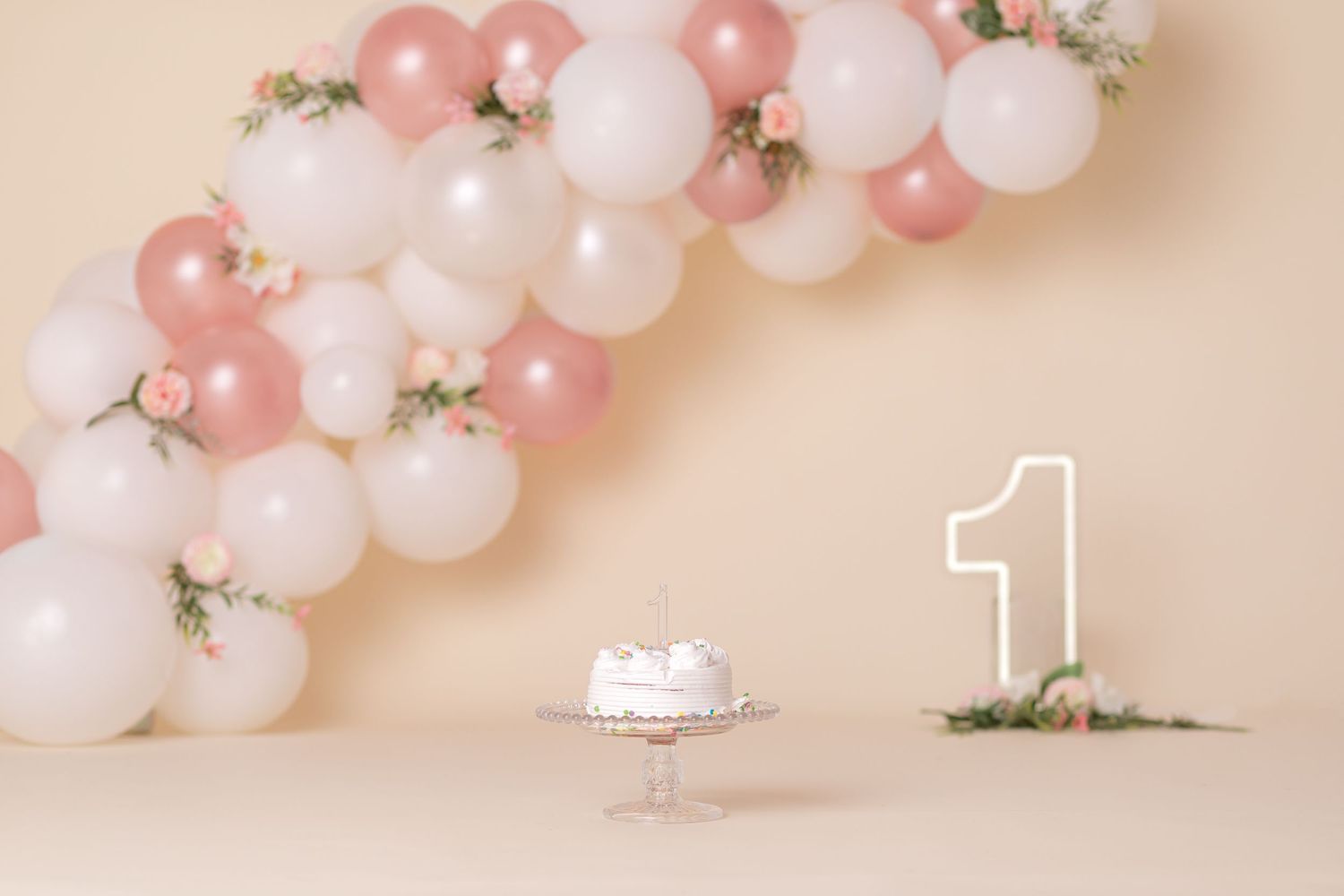 Pink and white balloon arch with number one decoration and small cake stand.
