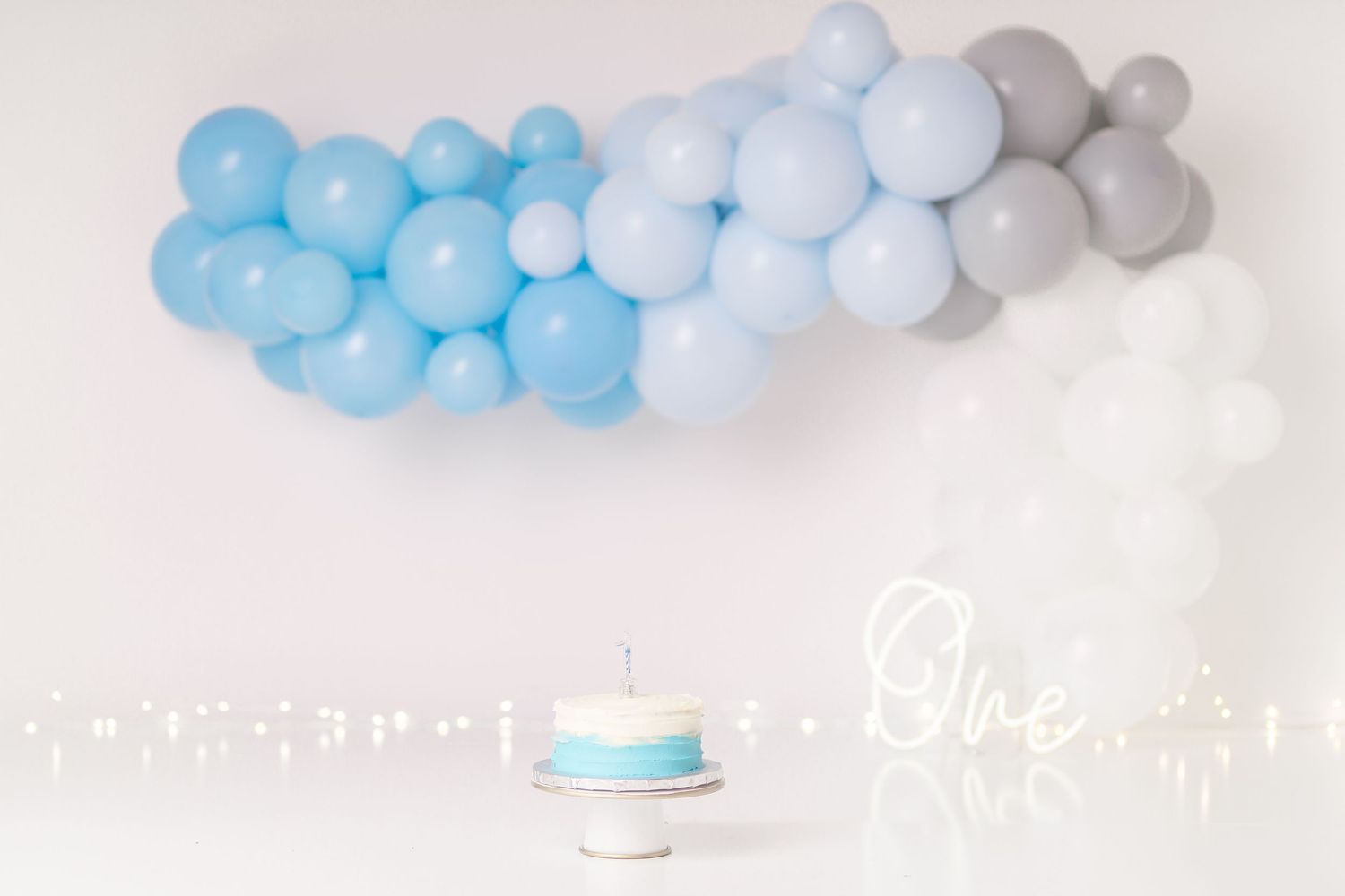 Blue and grey balloon arch installation with cake stand and white decorative elements.
