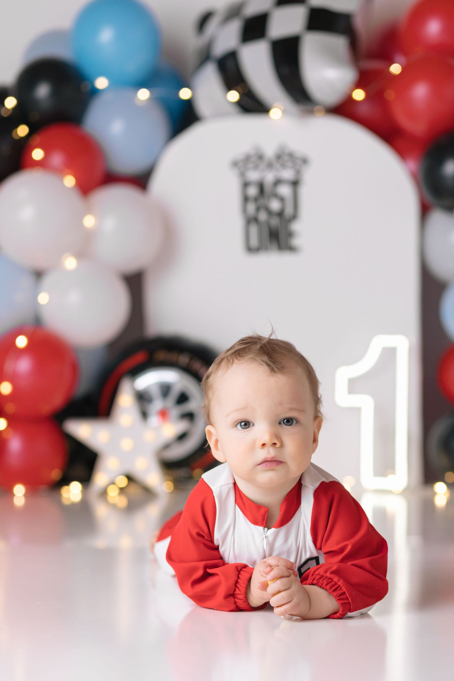 First birthday party setup with racing theme decorations featuring balloon arch in red, black, white and blue colors.