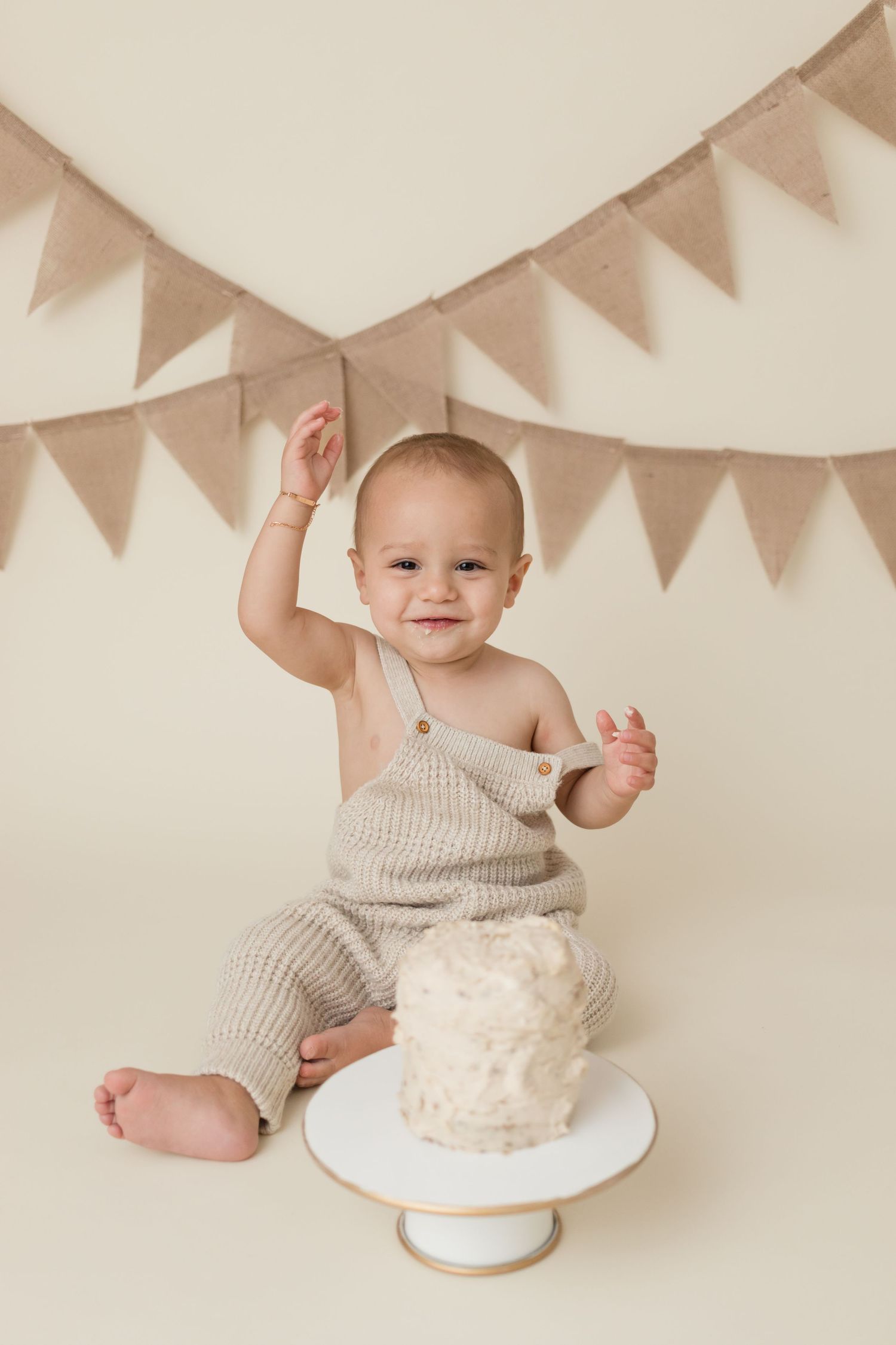 A minimalist first birthday setup with a white cake and neutral beige bunting decorations.