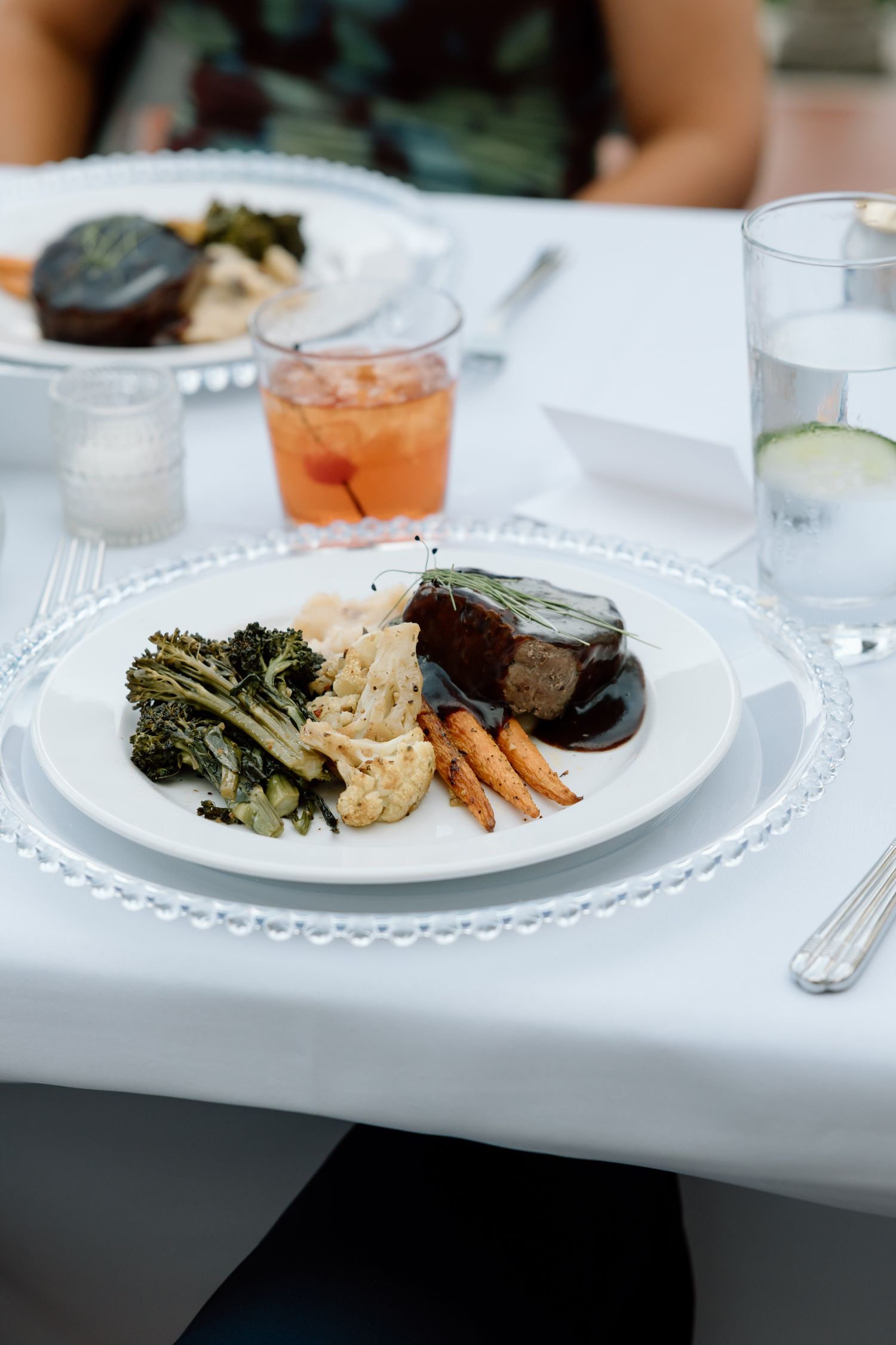 Elegant plated dinner with filet mignon, roasted carrots, broccoli, and cauliflower on a beaded charger plate.