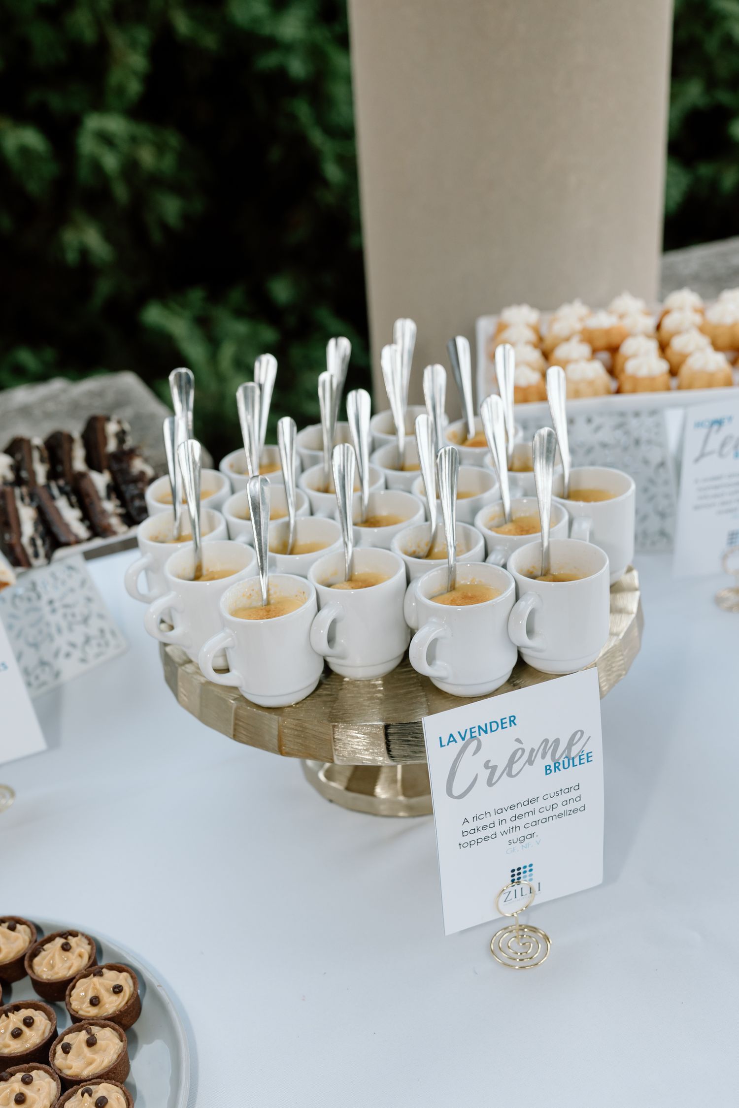 Dessert table display of mini lavender creme brulee cups with spoons on a gold cake stand.