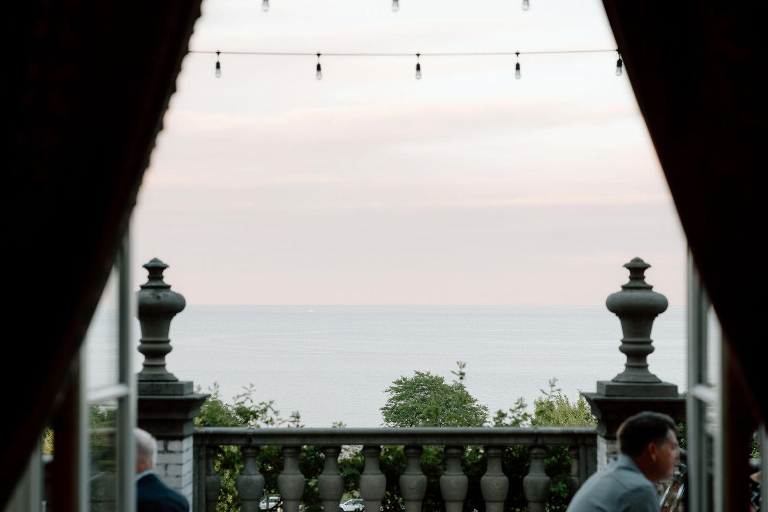 Romantic ocean view through arched doorway with stone balustrade at dusk wedding venue.