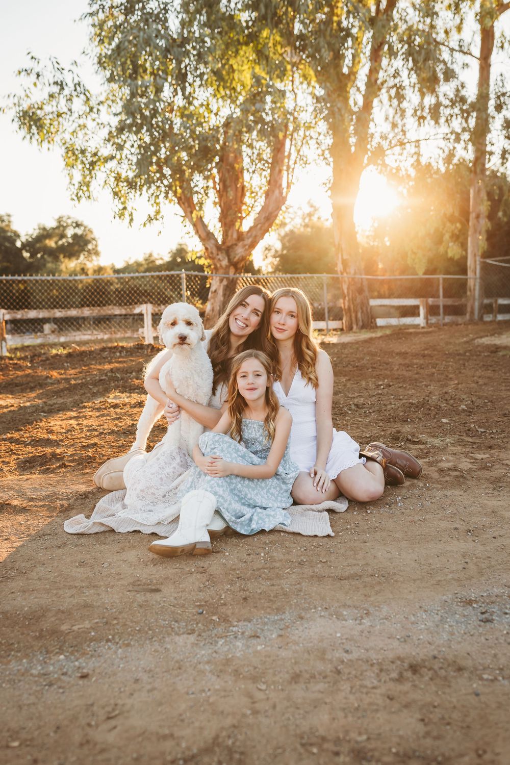 Two girls and a woman sit outdoors with a white fluffy dog at blooming ridge ranch in cherry valley ca