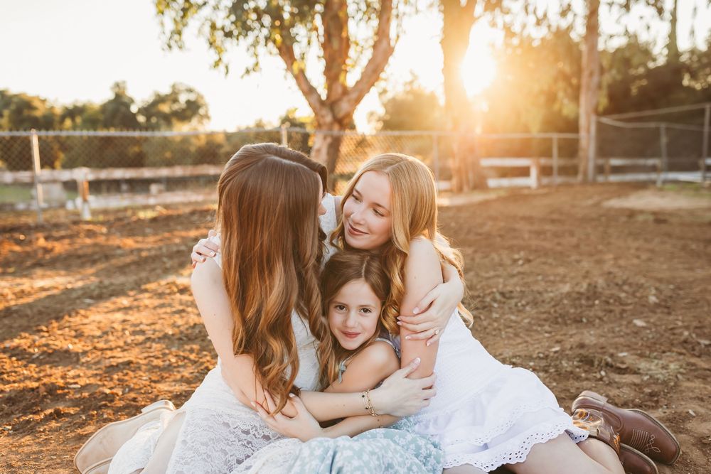 Three girls sitting together hugging warmly in golden sunset light with family photographer heidi grace photo