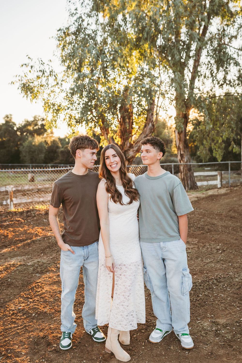 Three young adults pose together outdoors at golden hour near a large tree at blooming ridge ranch