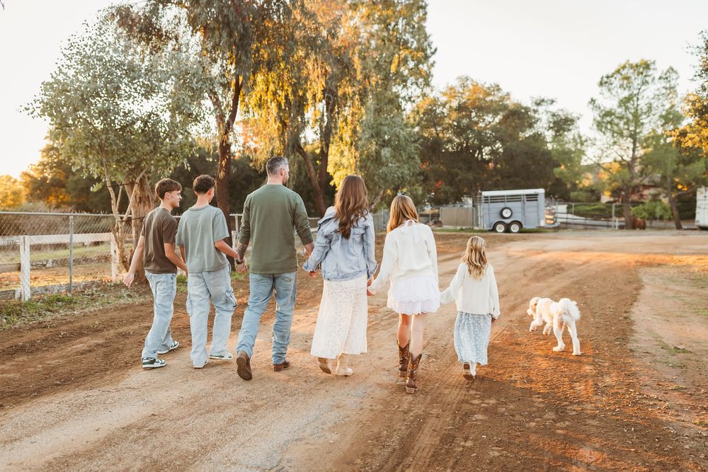 Family with dog walks down a dirt path at sunset on a scenic rural ranch property.