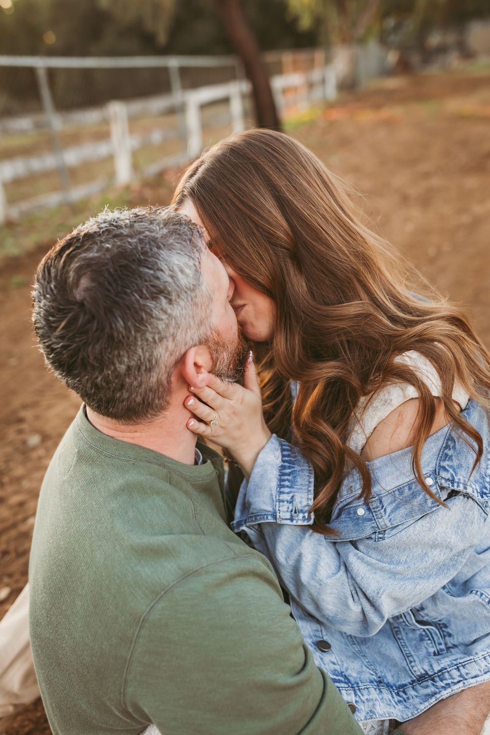 Couple sharing a tender kiss outdoors during golden hour near a white fence.