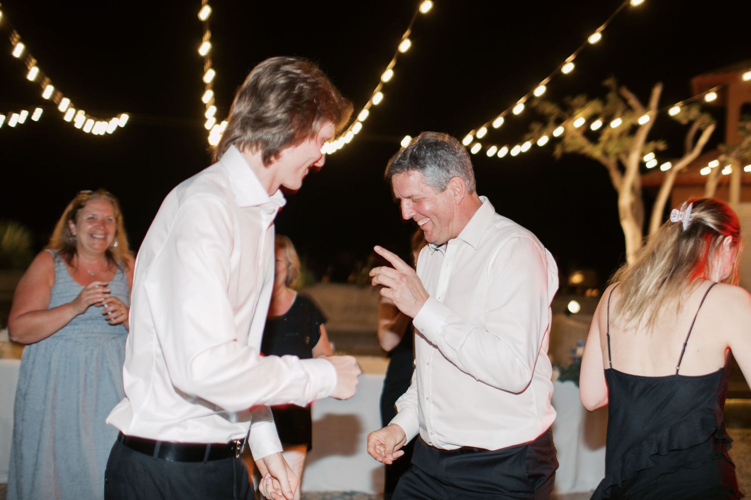 Bride in white lace gown dancing energetically with a guest at a wedding reception.
