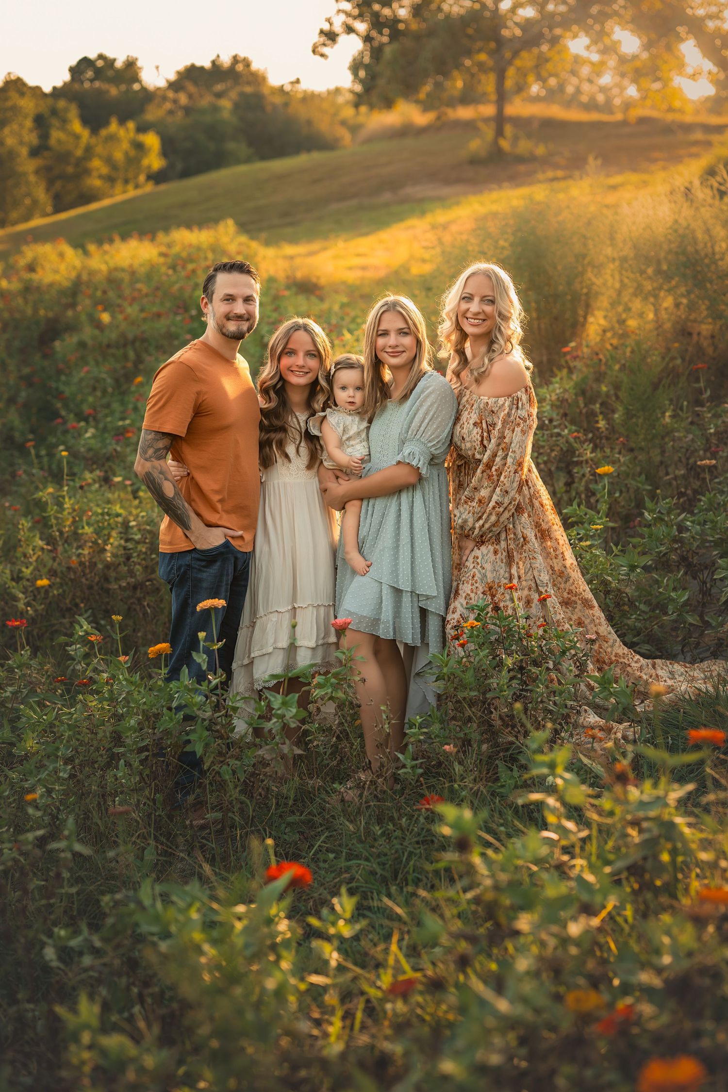 Family of five posing in a sunlit wildflower field during golden hour, wearing boho-style outfits.