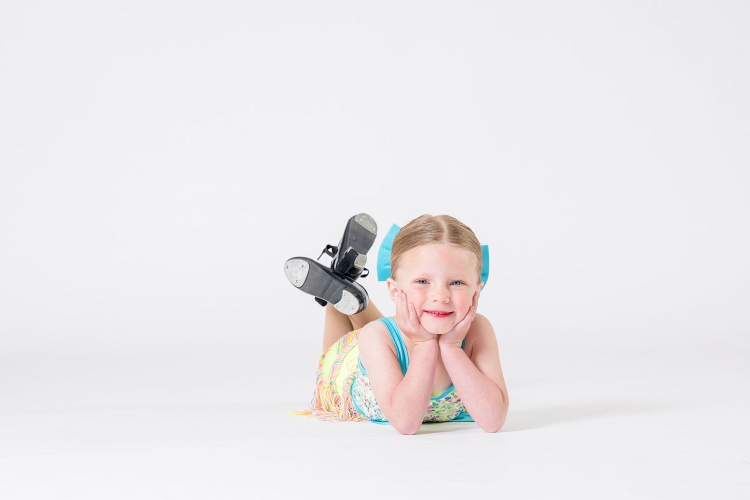 Smiling young girl lying on floor wearing colorful dress and roller blades with blue headphones.