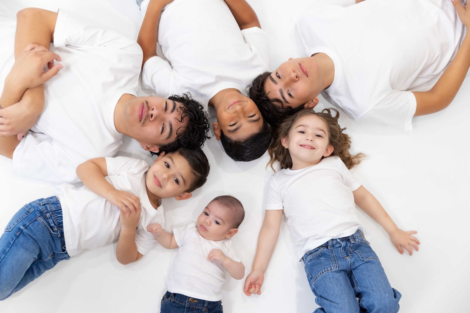 Happy family of six lying in circle on white background, including baby and young children.