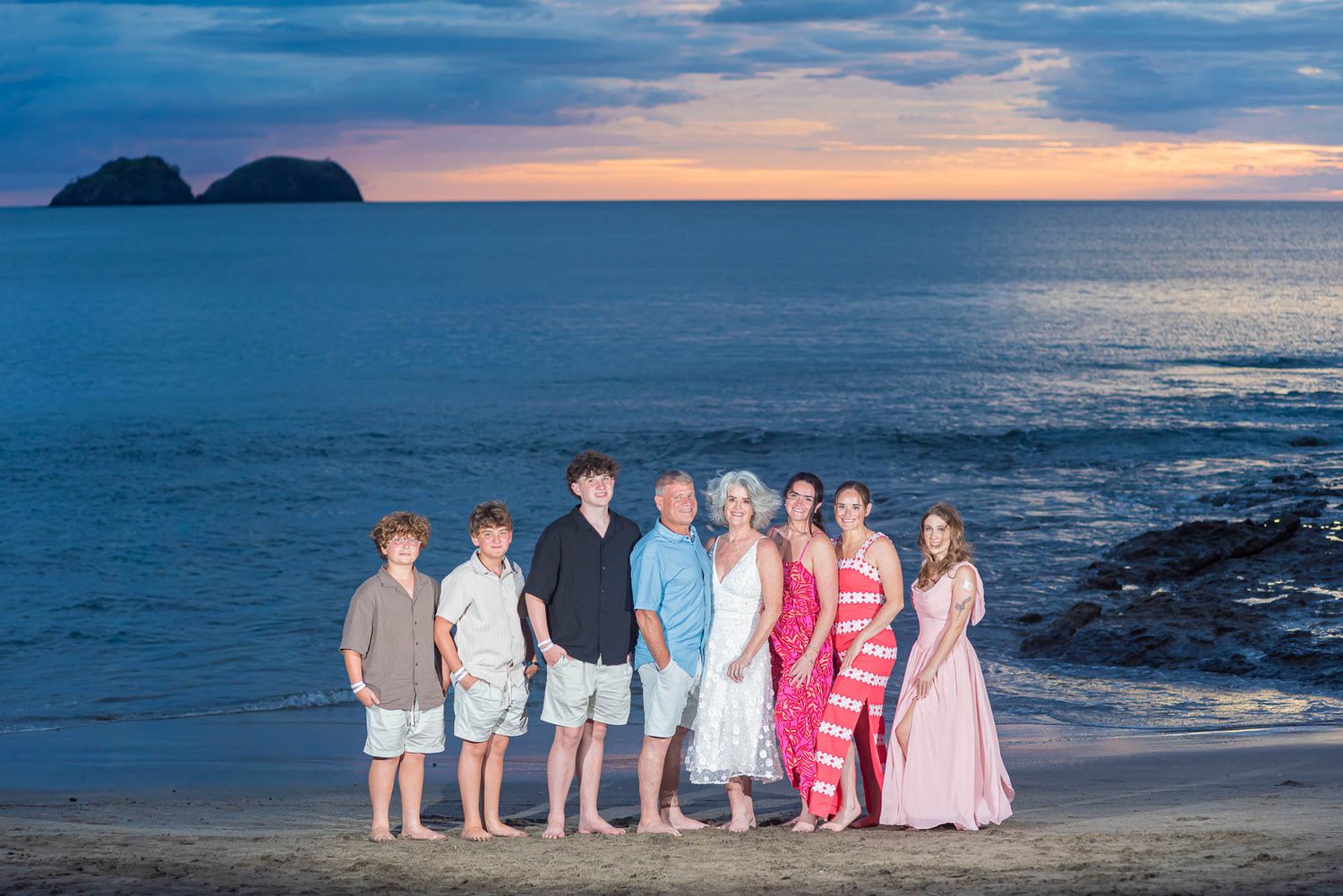 Happy family of six posing together on lush green lawn with tropical palm trees in sunny resort setting.