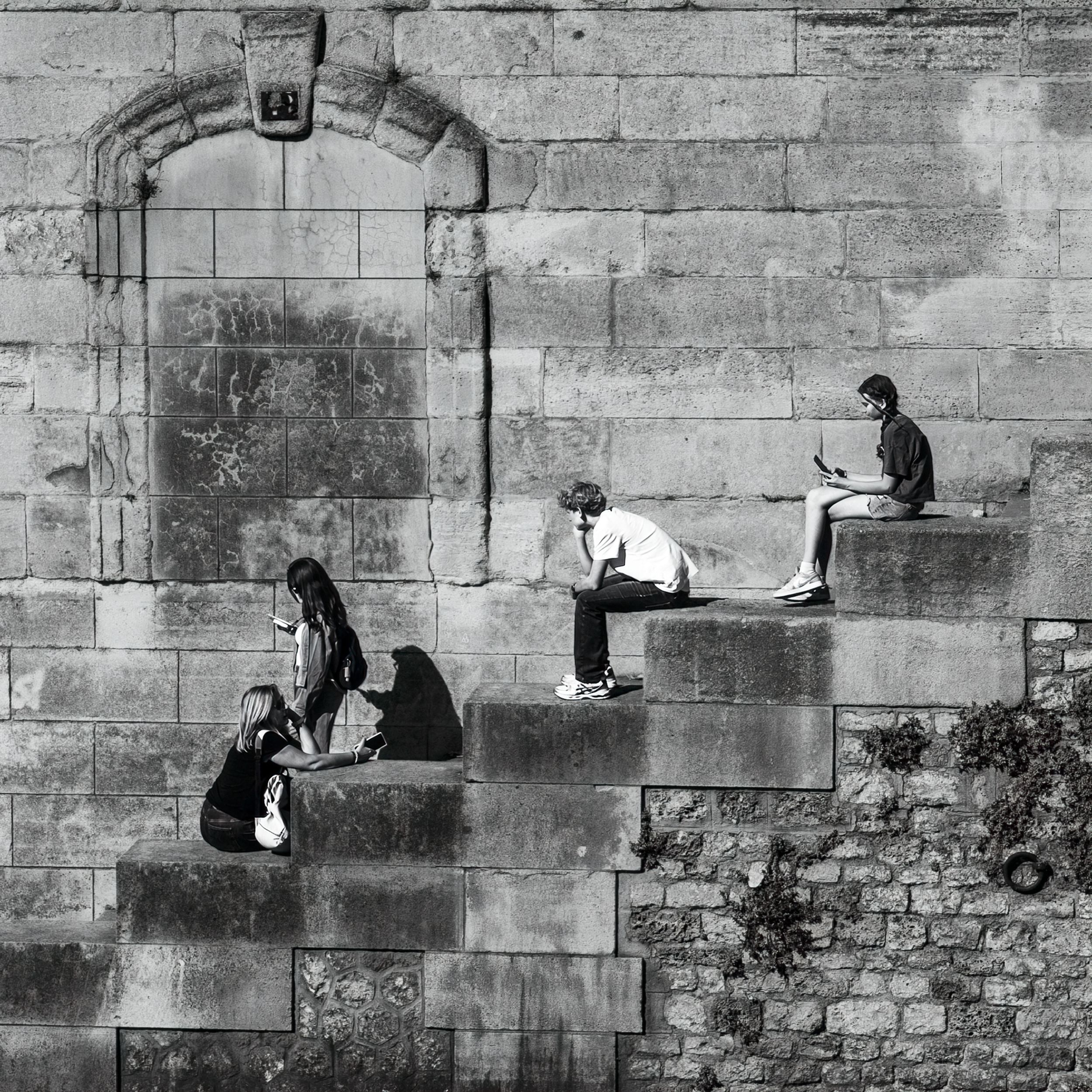 Black and white photo of people sitting on stepped stone wall ledges of an old historic building.