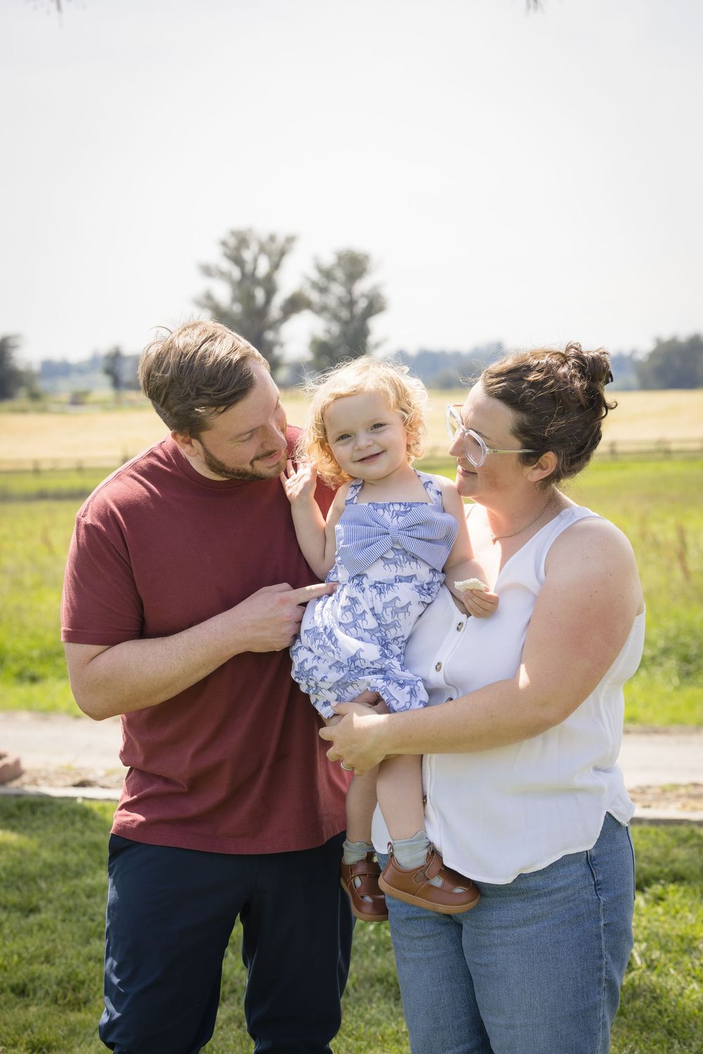 Happy family with parents holding their smiling toddler daughter in a blue dress outdoors.