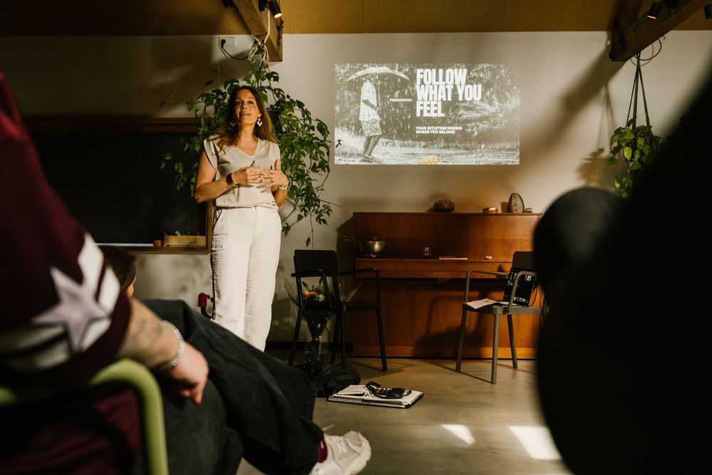 Woman presenting in front of a projected screen displaying Follow What You Feel in a cozy modern event space.