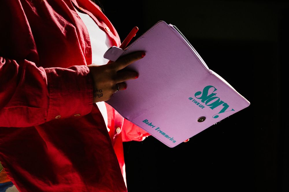 Person in red jacket holds a pink Story notebook in dramatic lighting.
