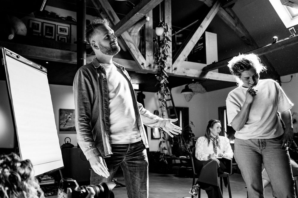 Black and white photo of people collaborating in a rustic workspace with exposed beams and a whiteboard.