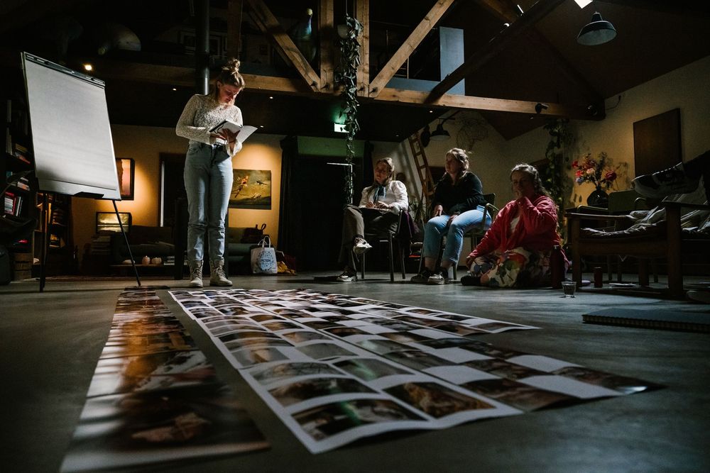 People reviewing photo prints spread on floor during creative workshop in rustic dimly lit studio space.